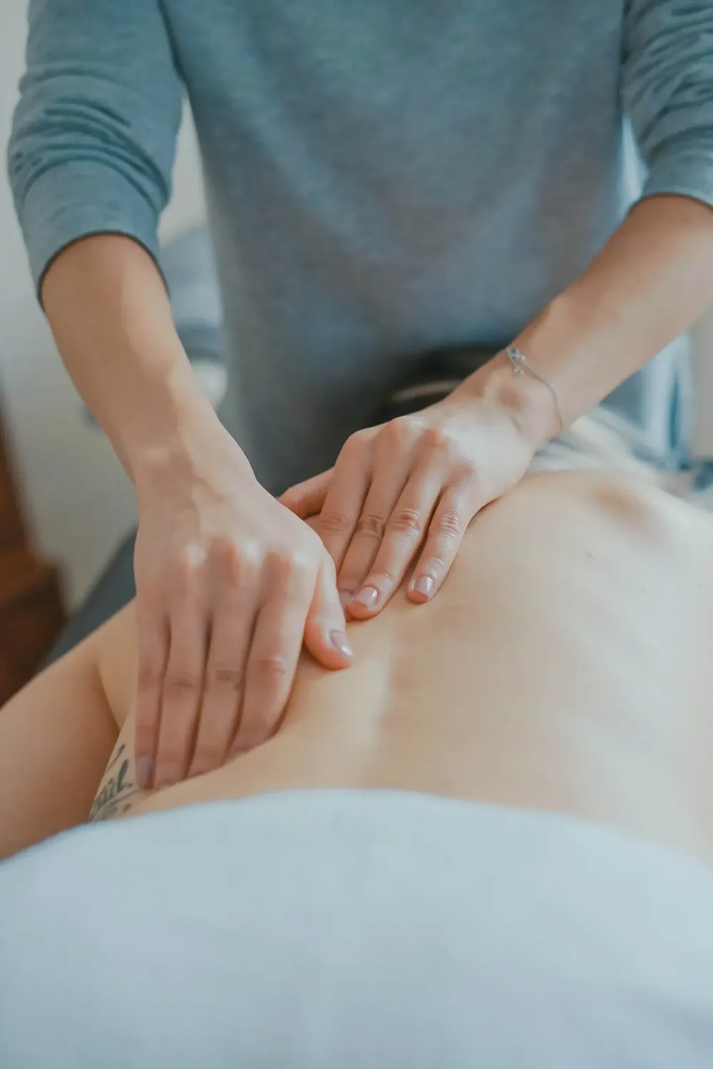 Körpermanufaktur - Physiotherapie. Osteopathie. Naturheilkunde – Dieses Bild zeigt eine Person, die in einer klinischen Umgebung eine therapeutische Massage erhält.